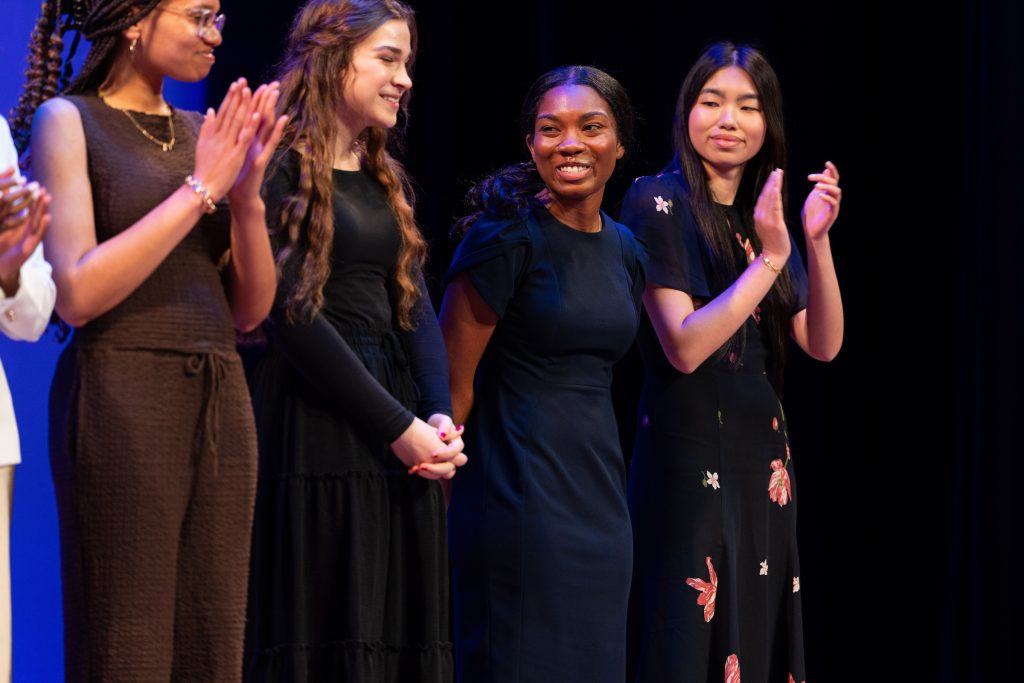 A group of students applaud for another student onstage.