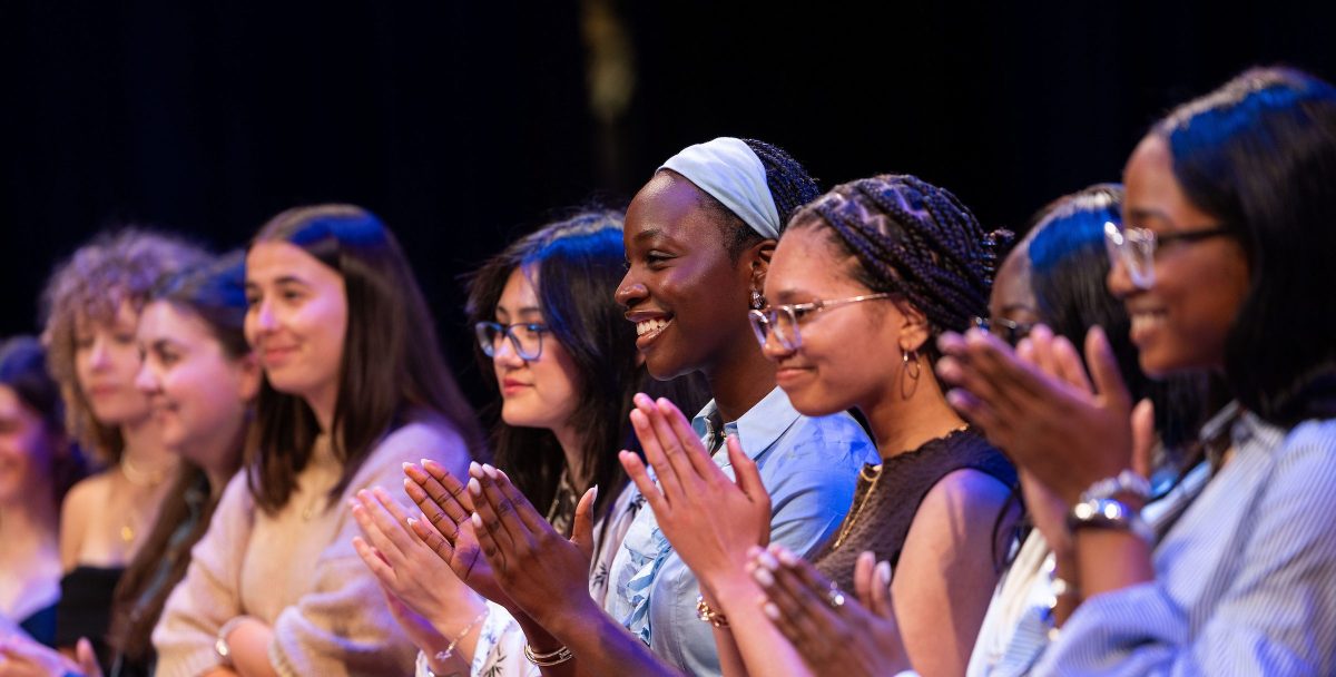 A group of student stand on stage and applaud.