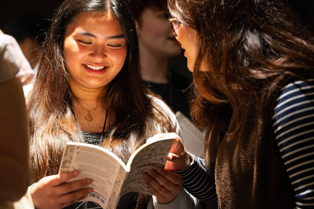 Two students talk while looking through a book of poetry.